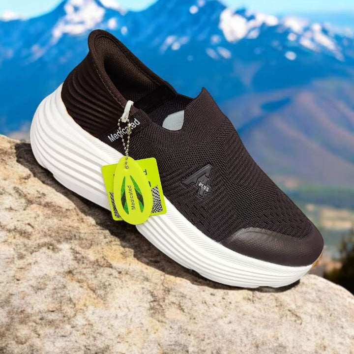 Black and white sneaker with a green tag on a rock with mountains in the background, labeled '100% Medicated'.